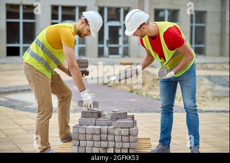 Skilled builders in cotton gloves choosing construction materials for pavement Stock Photo