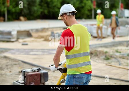 Worker in cotton gloves and a hardhat compacting the ground Stock Photo