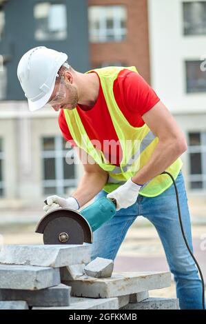 Concentrated worker in a hardhat and goggles leaning over construction materials Stock Photo