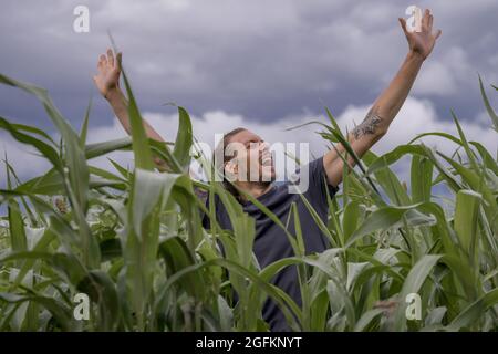 Young attractive man singing in a corn field, arms in the air, cloudy Stock Photo