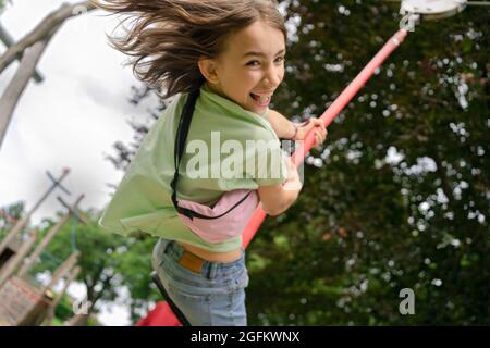 Happy girl laughingwhile swinging on rope on playground Stock Photo