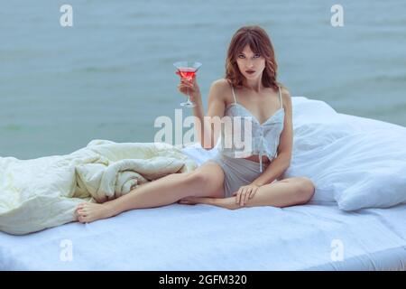 Woman sits on a bed that is on the water. The bed is on the ocean water. Stock Photo