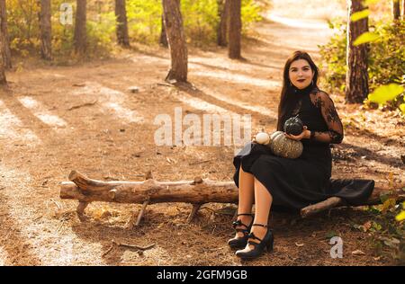 Young brunette female holding little pumpkins in front of her face, sitting in autumn forest background. Fall holidays, halloween decorations and peop Stock Photo