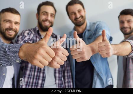 Group of happy positive young men standing together and showing thumbs up gesture Stock Photo