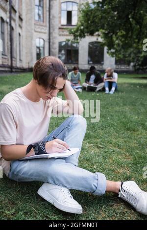 Student writing on notebook on lawn outdoors Stock Photo