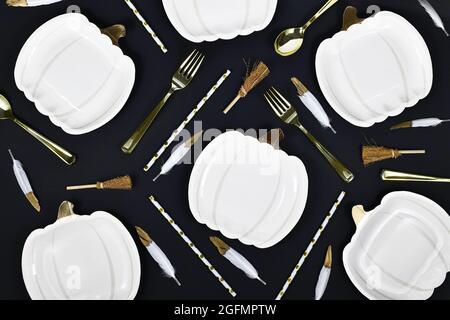 Halloween party flat lay with pumpkin shaped plates, brooms and golden forks and spoons on black background Stock Photo