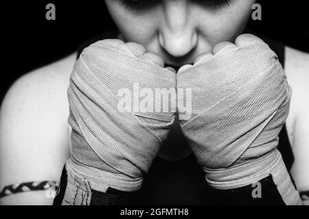 Muay Thai fighter girl preparing for battle. Closeup black and white portrait against black background. Stock Photo