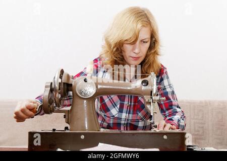Young red-haired woman stitching fabric using a old vintage sewing machine Stock Photo