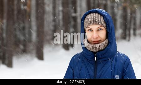 Portrait of a young woman surrounded by flying snowflakes on the background of a winter forest. Shallow focus. Stock Photo