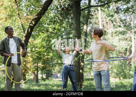 Teen boy with hula hoop pointing at african american friend in park Stock Photo