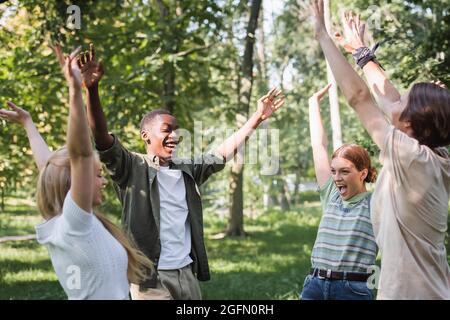 Excited multiethnic teenagers raising hands in park Stock Photo