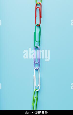 Interlocked colored paper clips in a line on a blue background with free space. The concept of unity Stock Photo