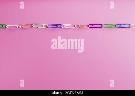 Multicolored paper clips are attached in a row on a pink background. Free space Stock Photo