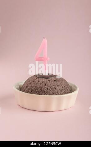 A small birthday cake with candle age four on pink Stock Photo
