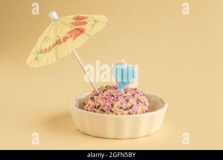 A small birthday cake with heart shaped candle and umbrella on yellow Stock Photo