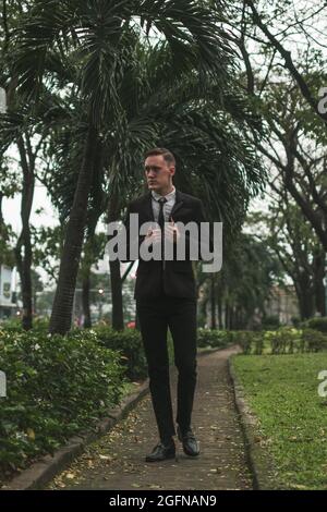 Attractive young business man in black formal suit walking in the park. Summer time. Serious look. High quality photo Stock Photo