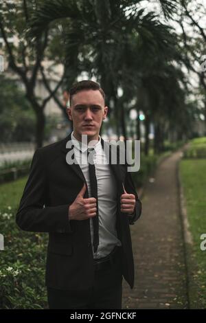 Portrait of attractive caucasian young entrepreneur in black formal suit outdoors. Looking at camera with copy space. Holding his jacket.  Stock Photo