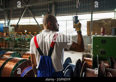 Engineer in uniform using crane controller hanging from ceiling in a factory Stock Photo