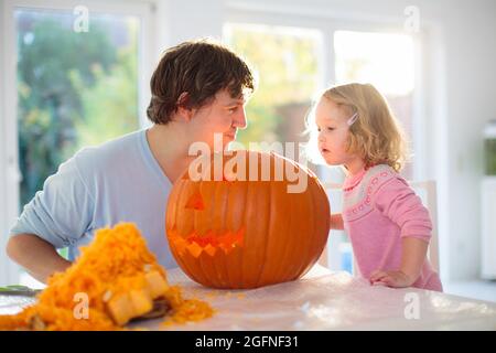 Father and child carving pumpkin for Halloween. Dad and little girl carve jack-o-lantern for trick or treat and home entrance decoration. Parents Stock Photo