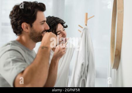 happy gay couple brushing teeth near mirror in bathroom Stock Photo