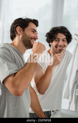 positive gay couple brushing teeth in bathroom Stock Photo