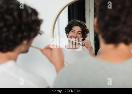 happy gay couple brushing teeth and looking at mirror in bathroom Stock Photo