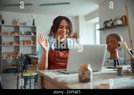 Cheerful female potter using laptop in pottery workshop Stock Photo