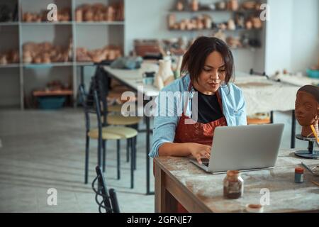 Charming female potter using notebook in pottery workshop Stock Photo