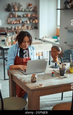 Charming female ceramist using laptop in pottery workshop Stock Photo