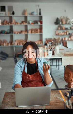 Joyful female potter using notebook in pottery workshop Stock Photo