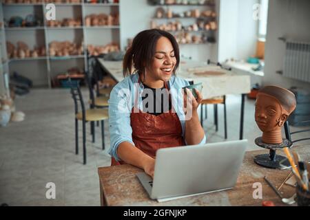 Cheerful female potter using notebook in pottery workshop Stock Photo