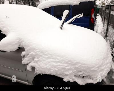 A silver-colored passenger car parked in a thick layer of snow on the roof Stock Photo