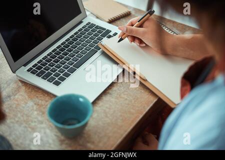 Female potter writing on notebook and using laptop in workshop Stock Photo
