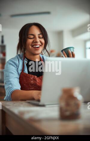 Cheerful female ceramist using laptop in pottery workshop Stock Photo