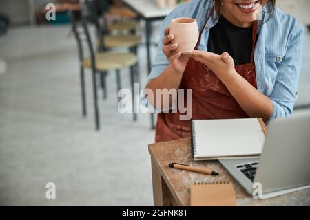 Joyful female potter using laptop in pottery workshop Stock Photo