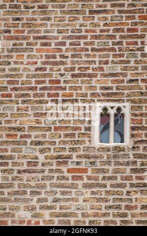 Brugge, Flanders, Belgium - August 4, 2021: Smallest spy window with stained glass in brown brick wall of Gruuthuse palace. Stock Photo