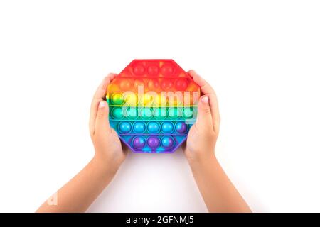 Child's hands holding colored pop it anti-stress toy isolated on white background. Close-up. Stock Photo
