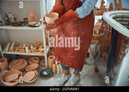 Female ceramist in gloves holding handmade clay bowl Stock Photo