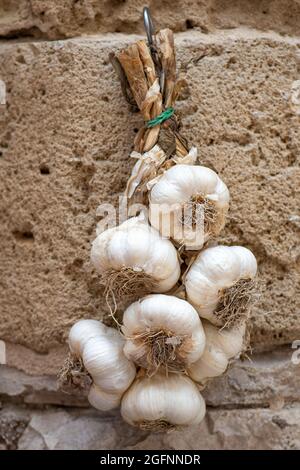 Bunch of white garlic hanging on a stone wall in a street food market, vertical Stock Photo
