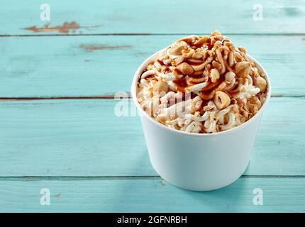 Hazelnut topping on a tub of vanilla ice cream spaghetti drizzled with caramel sauce for a tasty summer dessert viewed high angle with copyspace for m Stock Photo