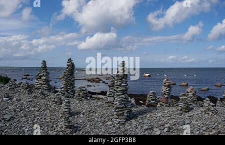 A rocky beach with many stone cairns and a calm ocean in the background Stock Photo