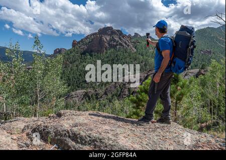Adventurous backpacker standing on a boulder pointing a camera towards the wilderness landscape Stock Photo