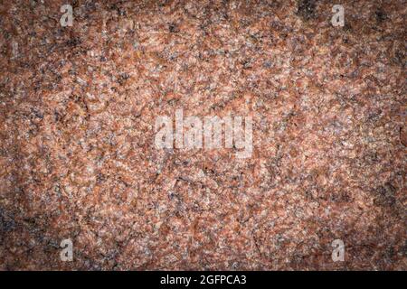 Dark red granite background, structured background with vignetting, darkening around the edges of the photo. Natural stone texture. Stock Photo