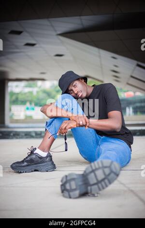 Vertical shot of a young afro-American man doing a sitting pose outside in France Stock Photo