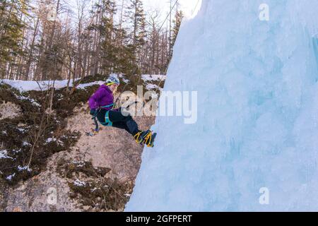 Female ice climber going down an ice waterfall, using a safety top rope. Stock Photo