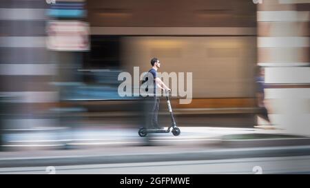 Charlotte, North Carolina, USA - August 24, 2021: Man with sunglasses rides scooter on sidewalk. Stock Photo