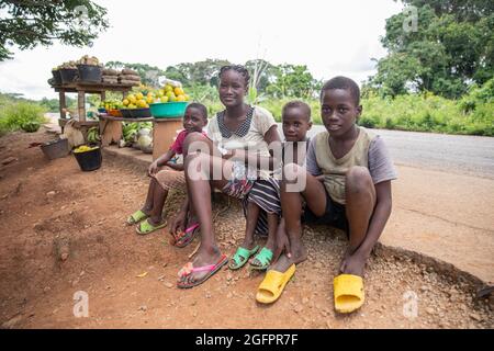 Group of African siblings sitting on the side of the road, they are poor and dressed in worn old clothes. they sell food on the street Stock Photo