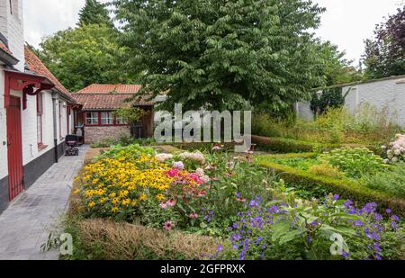 Brugge, Flanders, Belgium - August 4, 2021: Green garden with flowers of all colors as courtyard of Rooms Convent, medieval Godshuis, Guild sponsored Stock Photo