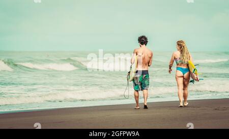 Playa Hermosa, Guanacaste, Costa Rica - 07.26.2020: A young man wearing shorts and a woman with blue bikinis are walking towards the sea