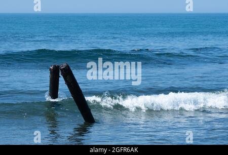 Waves crash and cover two wooden posts during high tide at Surfrider Beach, Malibu, California, USA Stock Photo